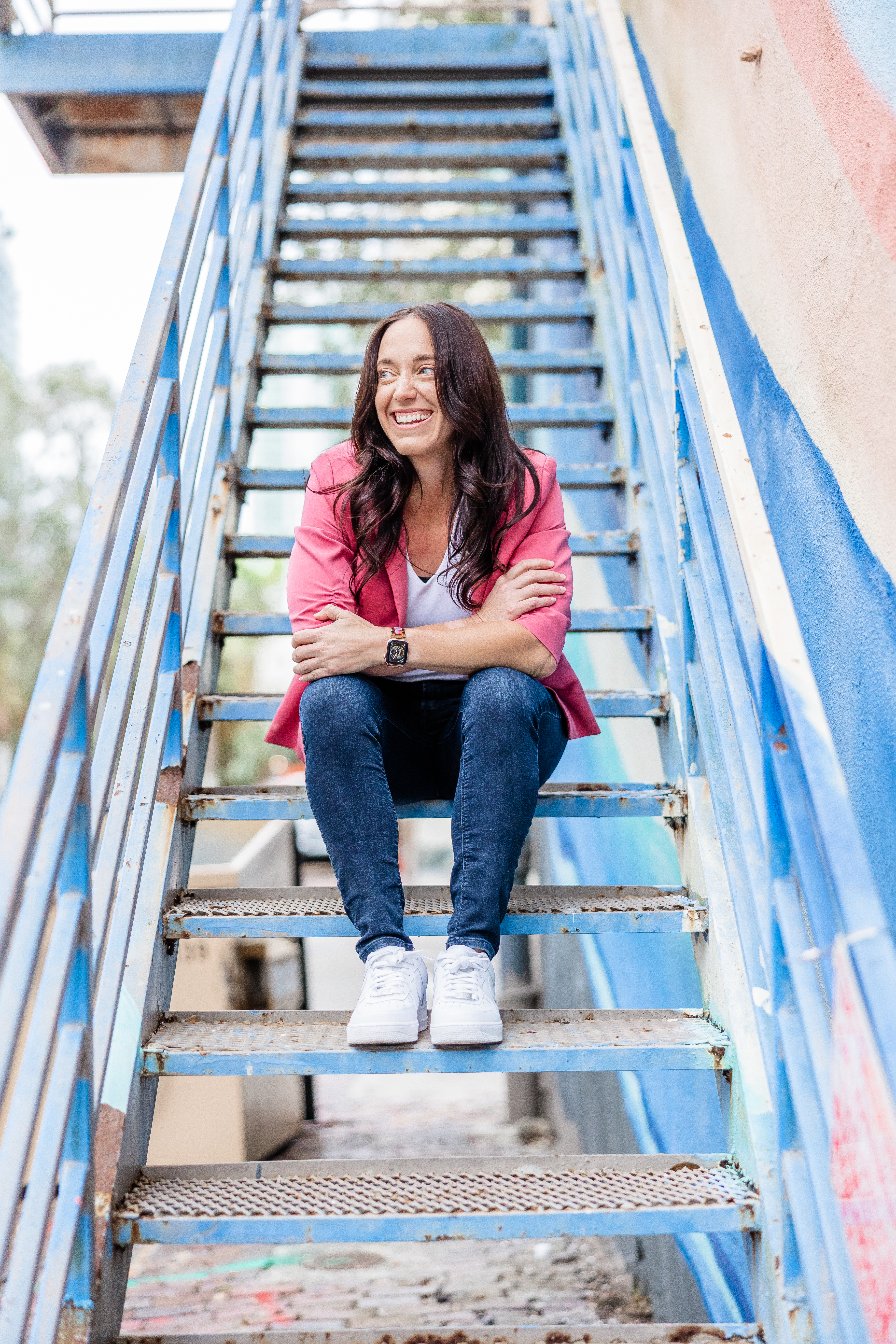 Kelly-Ann Jenkins, founder of Ascend Injury Law, sitting on blue industrial stairs in a pink blazer, smiling